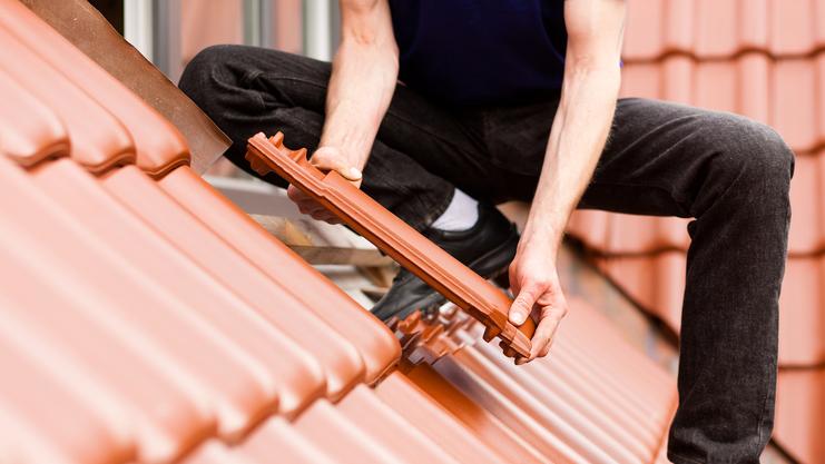 Handwerker platziert einen Dachziegel auf einem geneigten, roten Ziegeldach.